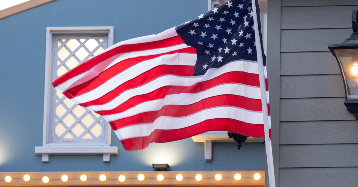 A large American flag being held up by an aluminum flagpole that is attached to the side of a green house.